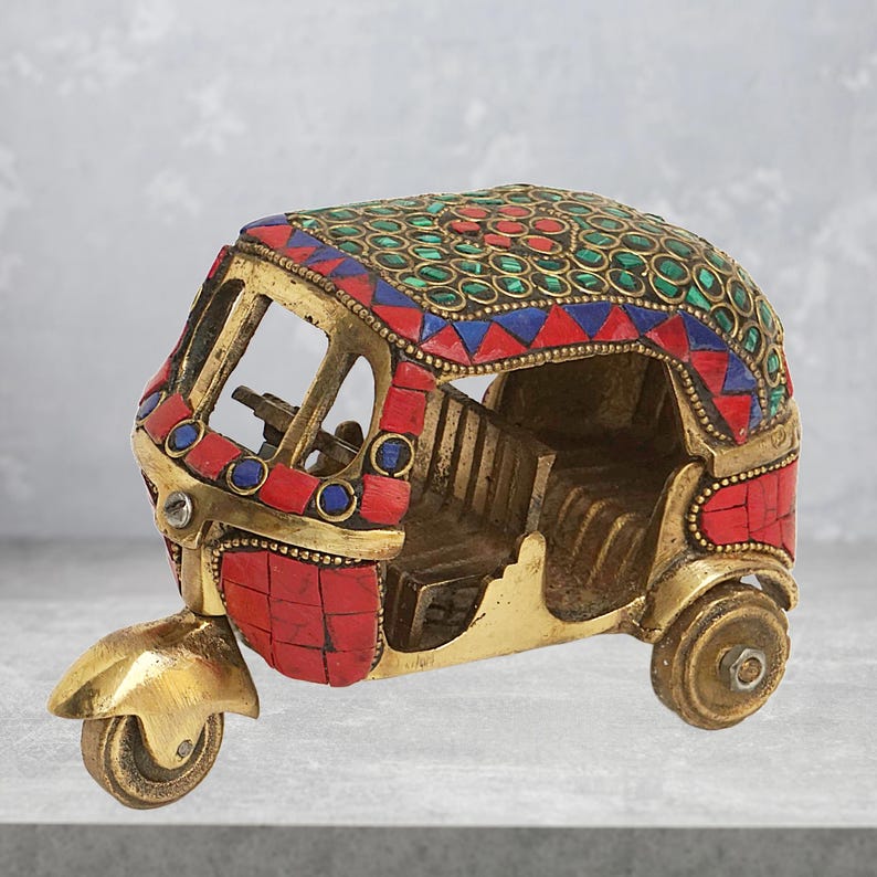 May include: A small, decorative brass auto rickshaw with red, blue, and green mosaic details. The rickshaw is a popular mode of transportation in India.