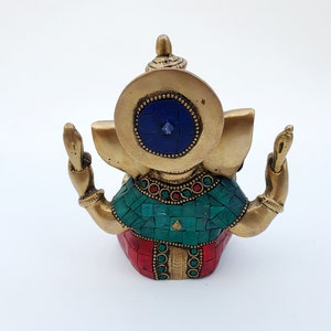 May include: A gold-colored brass statue of Ganesha, the Hindu god of wisdom and prosperity. The statue is decorated with red, green, and blue mosaic tiles and has a blue gemstone in the center of its forehead.