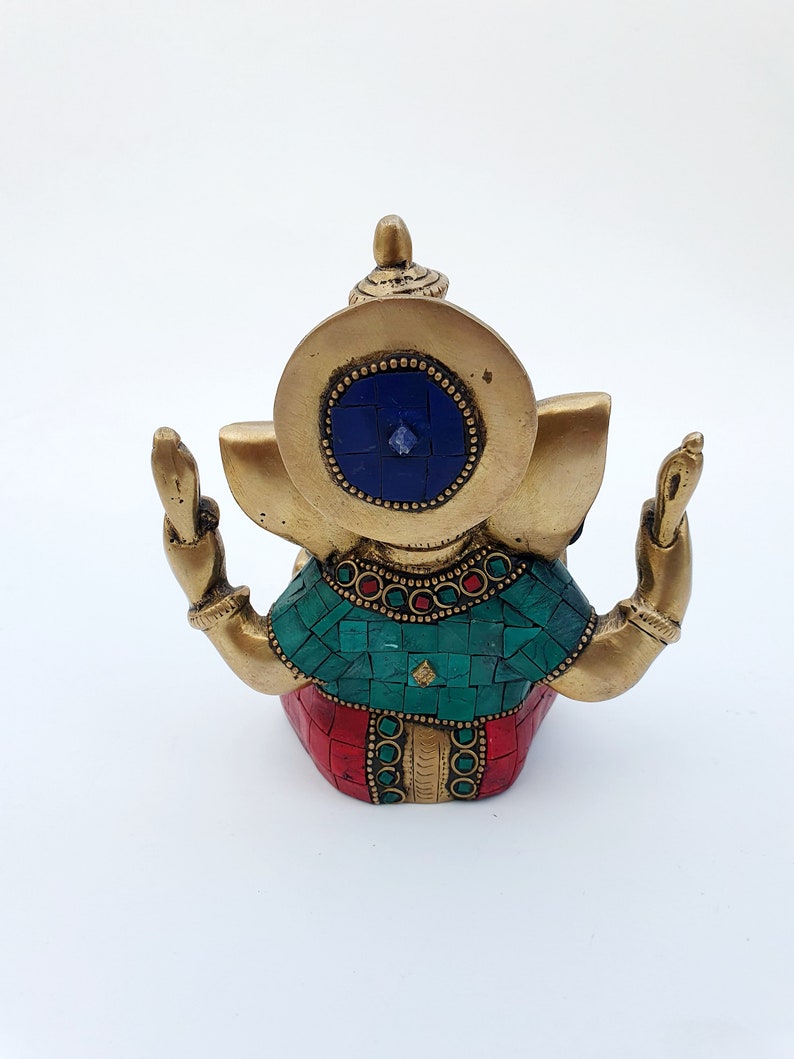 May include: A gold-colored brass statue of Ganesha, the Hindu god of wisdom and prosperity. The statue is decorated with red, green, and blue mosaic tiles and has a blue gemstone in the center of its forehead.