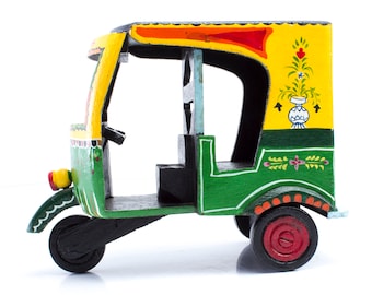May include: A hand-painted wooden toy auto rickshaw, also known as a tuk-tuk, with a green body, yellow roof, and red accents. The toy features intricate floral designs and a black steering wheel.