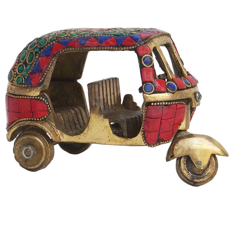 May include: A small, gold-colored metal model of an auto rickshaw, also known as a tuk-tuk, decorated with red, blue, and green mosaic tiles.