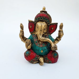May include: A gold-colored brass statue of Ganesha, the Hindu god of beginnings, prosperity, and good fortune. The statue is decorated with red and green gemstones and has a detailed design.