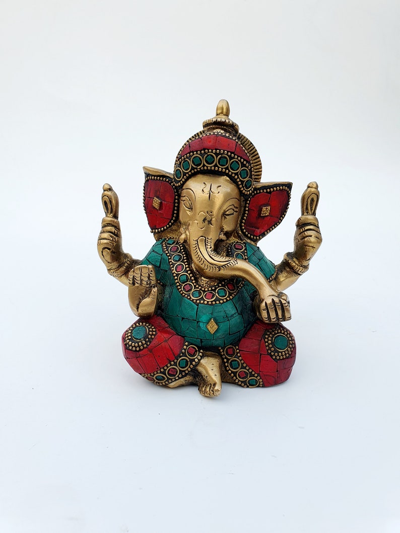 May include: A gold-colored brass statue of Ganesha, the Hindu god of beginnings, prosperity, and good fortune. The statue is decorated with red and green gemstones and has a detailed design.