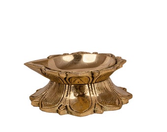 Könnte beinhalten: Eine goldfarbene Messing-Diya, oder Öllampe, mit einem dekorativen Lotusblüten-Design. Die Diya hat eine runde Schale für Öl und einen breiten Standfuß.