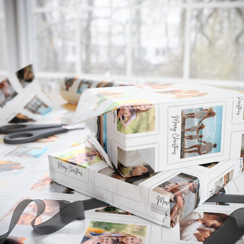 May include: Two gift boxes wrapped in white paper printed with family photos and the words "Merry Christmas." A black ribbon and scissors are on the table. The boxes are partially unwrapped.