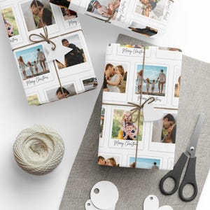 May include: White wrapping paper featuring a collage of family photos in a polaroid style. The paper is tied with twine and a star-shaped tag. The words "Merry Christmas" are written on the paper. A ball of twine, scissors, and blank tags are also visible.