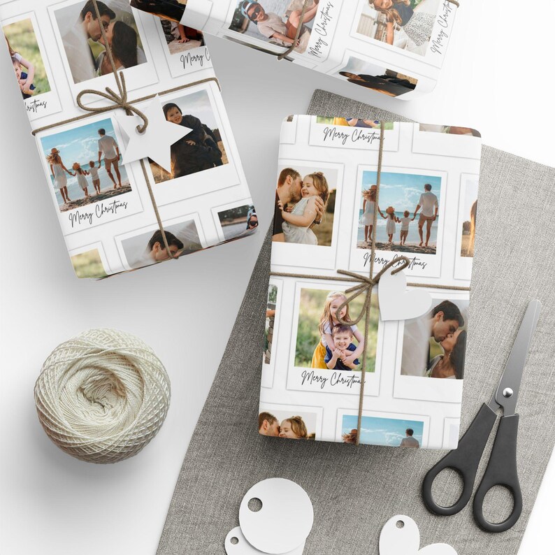 May include: White wrapping paper featuring a collage of family photos in a polaroid style. The paper is tied with twine and a star-shaped tag. The words "Merry Christmas" are written on the paper. A ball of twine, scissors, and blank tags are also visible.