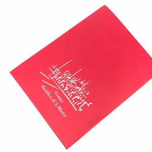 Puede incluir: Una tarjeta roja con un contorno blanco de la Bas&iacute;lica de San Marcos en Venecia, Italia. El texto "Venecia Basilica di S. Marco" est&aacute; escrito debajo del contorno.