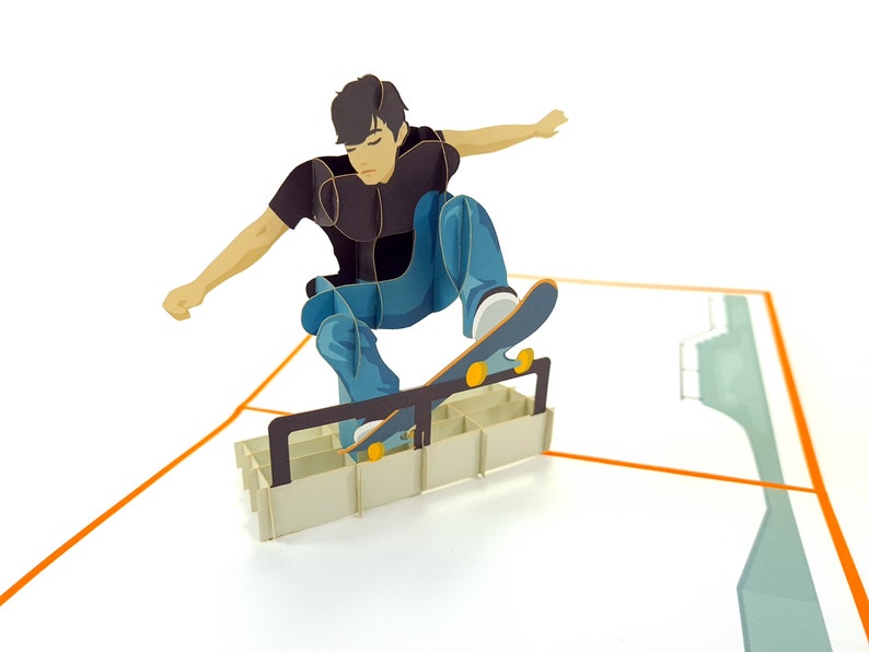 May include: A pop-up card featuring a person skateboarding over a ramp made of cardboard. The person is wearing a black shirt and blue jeans. The skateboard is brown with yellow wheels.