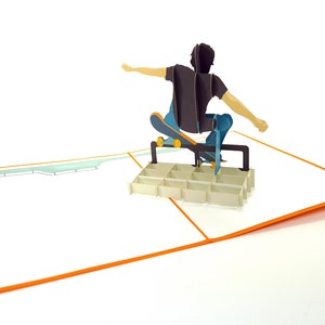 May include: A pop-up card featuring a person skateboarding over a ramp. The card is open and the person is in mid-air, with the skateboard wheels touching the ramp. The card is white with an orange border.