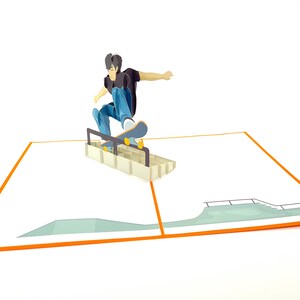 May include: A 3D pop-up card featuring a person skateboarding over a ramp. The card is open and the person is in mid-air, with their skateboard wheels touching the ramp. The card is on a white background.