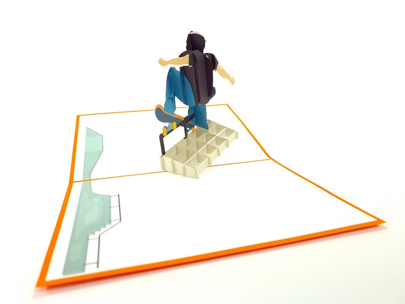 May include: A 3D pop-up card featuring a person skateboarding on a ramp. The card is open and the person is in mid-air, with their skateboard wheels touching the ramp. The card is white with an orange border.