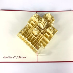 Puede incluir: Una tarjeta de papel pop-up beige con un modelo 3D de la Bas&iacute;lica de San Marcos en Venecia, Italia. La tarjeta est&aacute; abierta y el modelo est&aacute; completamente extendido. La tarjeta tiene un borde rojo.