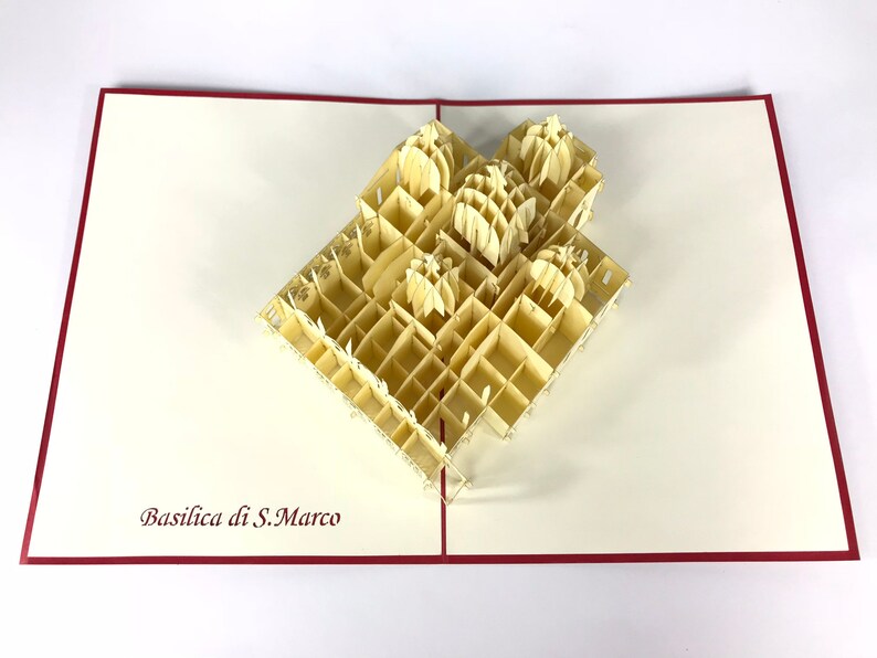Puede incluir: Una tarjeta de papel pop-up beige con un modelo 3D de la Bas&iacute;lica de San Marcos en Venecia, Italia. La tarjeta est&aacute; abierta y el modelo est&aacute; completamente extendido. La tarjeta tiene un borde rojo.