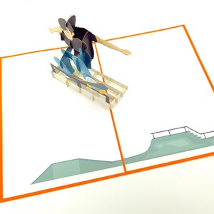May include: A pop-up card featuring a person skateboarding on a ramp. The card is open and the person is in mid-air, with the skateboard underneath them. The card is white with an orange border and a green ramp.