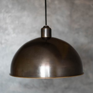 May include: A black metal pendant light with a dome-shaped shade and a brass trim. The light is hanging from a black cord.