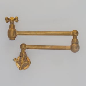 Może przedstawiać: Złoty mosiężny kran kuchenny z obrotowym wylewką i dwoma uchwytami. Kran jest zamontowany na ścianie.