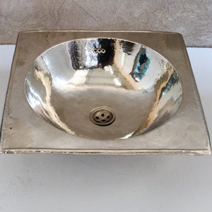 May include: A square, silver-colored bathroom sink with a rounded bowl and a drain in the center.