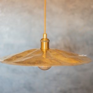 May include: A gold pendant light with a hammered metal shade. The light is hanging from a ceiling and has a single light bulb.