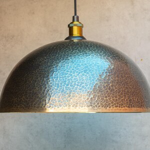 Puede incluir: Una l&aacute;mpara colgante de metal martillado con una pantalla en forma de c&uacute;pula. La pantalla es de color bronce oscuro con una p&aacute;tina azul claro. La l&aacute;mpara tiene un dise&ntilde;o simple e industrial.