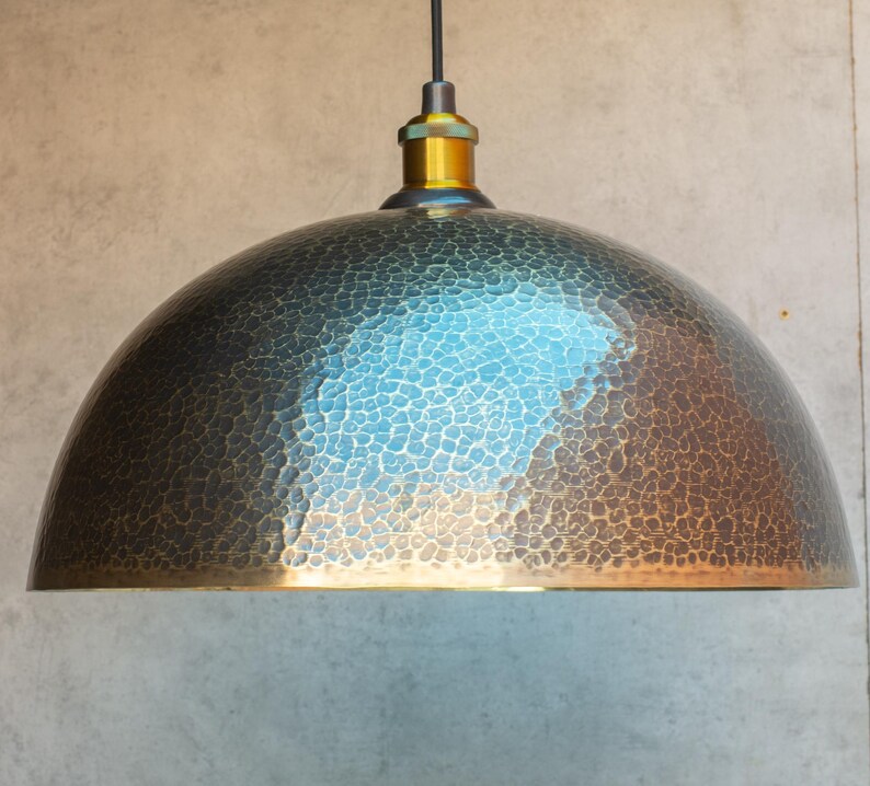 Puede incluir: Una l&aacute;mpara colgante de metal martillado con una pantalla en forma de c&uacute;pula. La pantalla es de color bronce oscuro con una p&aacute;tina azul claro. La l&aacute;mpara tiene un dise&ntilde;o simple e industrial.