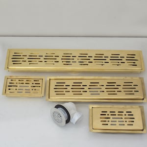 May include: Four gold-colored metal drain covers of varying sizes, with a smaller white plastic drain stopper with a decorative design.