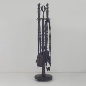 May include: A black fireplace tool set with a round base and a central stand holding a poker, shovel, brush, and tongs. The tools have decorative handles and are arranged vertically. The set is made of metal.