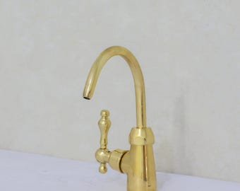 May include: A gold-colored faucet with a curved spout and a decorative handle. The faucet has a classic design and is made of a shiny, metallic material. The spout curves downward, and the handle has a detailed, ornate design.