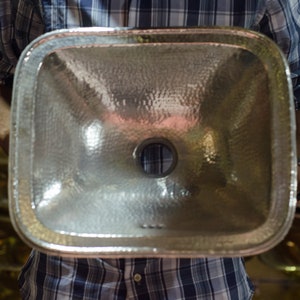 May include: A hammered silver rectangular bathroom sink with a drain hole in the center.