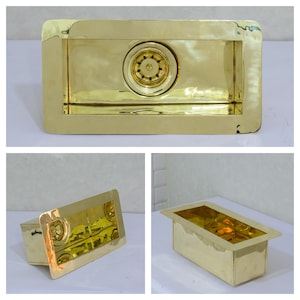 Op de afbeelding: Een rechthoekige gootsteen in goudkleur met een afvoer in het midden. De gootsteen is gemaakt van metaal en heeft een gehamerde afwerking.