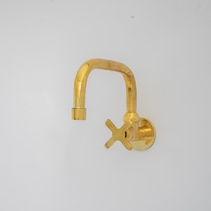 Puede incluir: Un grifo de color dorado con un caño curvo y una manija en forma de cruz. El grifo está montado en una pared.