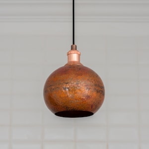 May include: A copper pendant light fixture with a hammered texture. The round shade is suspended from a black cord and a copper-colored base. The light fixture is designed to be hung from the ceiling.