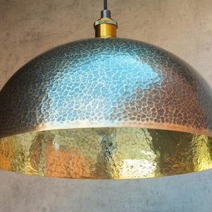 Puede incluir: Una l&aacute;mpara colgante de c&uacute;pula de metal martillado con acabado en lat&oacute;n. La luz tiene una superficie texturizada y un interior dorado.
