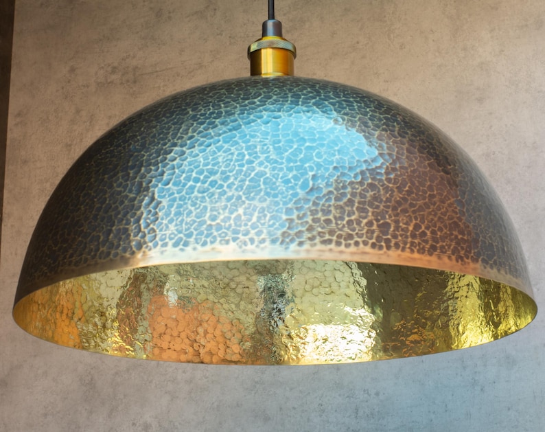 Puede incluir: Una l&aacute;mpara colgante de c&uacute;pula de metal martillado con acabado en lat&oacute;n. La luz tiene una superficie texturizada y un interior dorado.