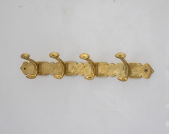 May include: A gold metal coat rack with four hooks. The rack has a decorative design with a scalloped edge.