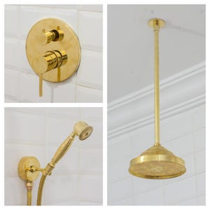 May include: A collection of gold bathroom fittings, including a shower head, handheld shower, and wall-mounted controls. The shower head is circular with a flat, perforated surface. The fittings are mounted on white tiled walls.