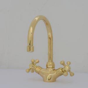 May include: A gold-toned kitchen faucet with a high-arc spout and two cross-shaped handles.