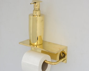 Könnte beinhalten: Vergoldetes Badezimmer-Set mit einem Seifenspender und einem Toilettenpapierhalter. Der Spender ist auf einem Regal montiert und der Halter ist unter dem Regal montiert.