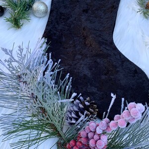May include: A black velvet stocking with a white fluffy background. The stocking is decorated with a pine sprig and red berries.