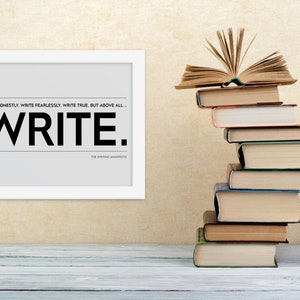 May include: A framed print with the text "WRITE HONESTLY WRITE FEARLESSLY WRITE TRUE. BUT ABOVE ALL... WRITE. THE WRITING MANIFESTO" on a gray background. A stack of books with an open book on top is in the background.