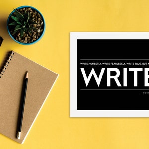 May include: A black and white motivational poster with the text "WRITE HONESTLY. WRITE FEARLESSLY. WRITE TRUE. BUT ABOVE ALL... WRITE." and the words "THE WRITING MANIFESTO" at the bottom. The poster is framed in white and is sitting on a yellow surface.