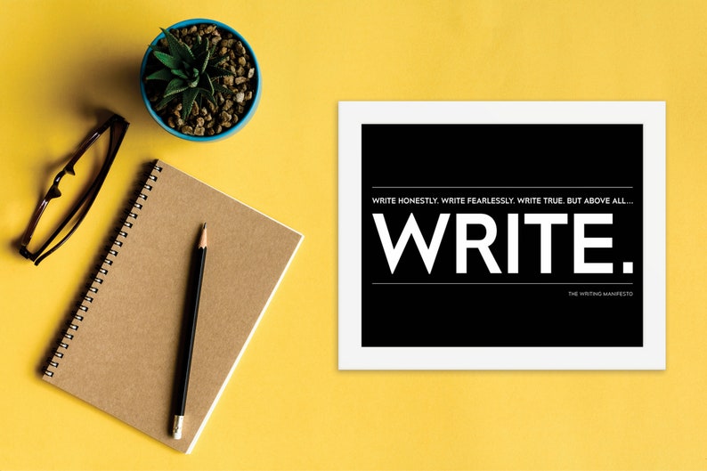 May include: A black and white motivational poster with the text "WRITE HONESTLY. WRITE FEARLESSLY. WRITE TRUE. BUT ABOVE ALL... WRITE." and the words "THE WRITING MANIFESTO" at the bottom. The poster is framed in white and is sitting on a yellow surface.