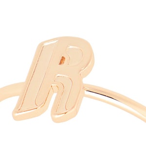 May include: A gold-toned ring featuring the letter "R" in a bold, stylised font.