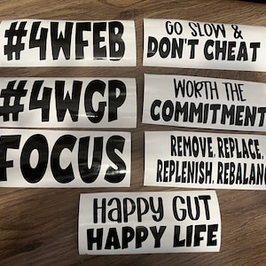 May include: A collection of white vinyl stickers with black text. The stickers feature motivational phrases such as "Go Slow & Don't Cheat", "Worth the Commitment", and "Happy Gut Happy Life". Other stickers have hashtags and the word "Focus".