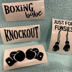 May include: Four white vinyl decals with black text and graphics. The decals read "BOXING babe", "KNOCKOUT", and "JUST FOR FUNSIES" with boxing glove graphics. The fourth decal features two black boxing gloves.