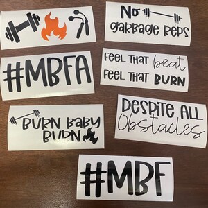May include: A set of seven white vinyl stickers with black text and graphics. The stickers feature motivational phrases related to fitness, including "#MBFA", "No garbage reps", "Feel that beat, feel that burn", "Burn baby burn", "Despite all obstacles", and "#MBF".