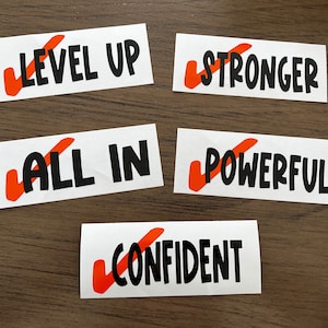 May include: Five white cards with orange checkmarks and black text. The cards read "Level Up", "Stronger", "All In", "Powerful", and "Confident".