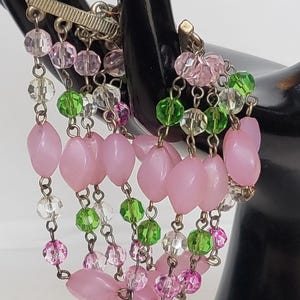 May include: A multi-strand bracelet featuring pink, green, and clear beads. The bracelet has a toggle clasp and is composed of various shapes and sizes of beads, including oval and round. The beads are strung on delicate chains.
