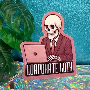 Może przedstawiać: Naklejka przedstawiająca szkielet w garniturze, pracujący na laptopie. Naklejka ma różową obwódkę i napis "CORPORATE GOTH" białymi literami. Tło jest błyszczące, turkusowe.