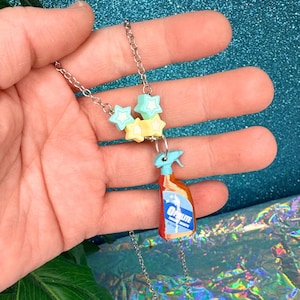May include: A silver chain necklace with star-shaped beads in pastel colors and a miniature cleaning spray bottle pendant. The bottle is orange and blue with the word "Oplite" on the label. The necklace is held in a hand.